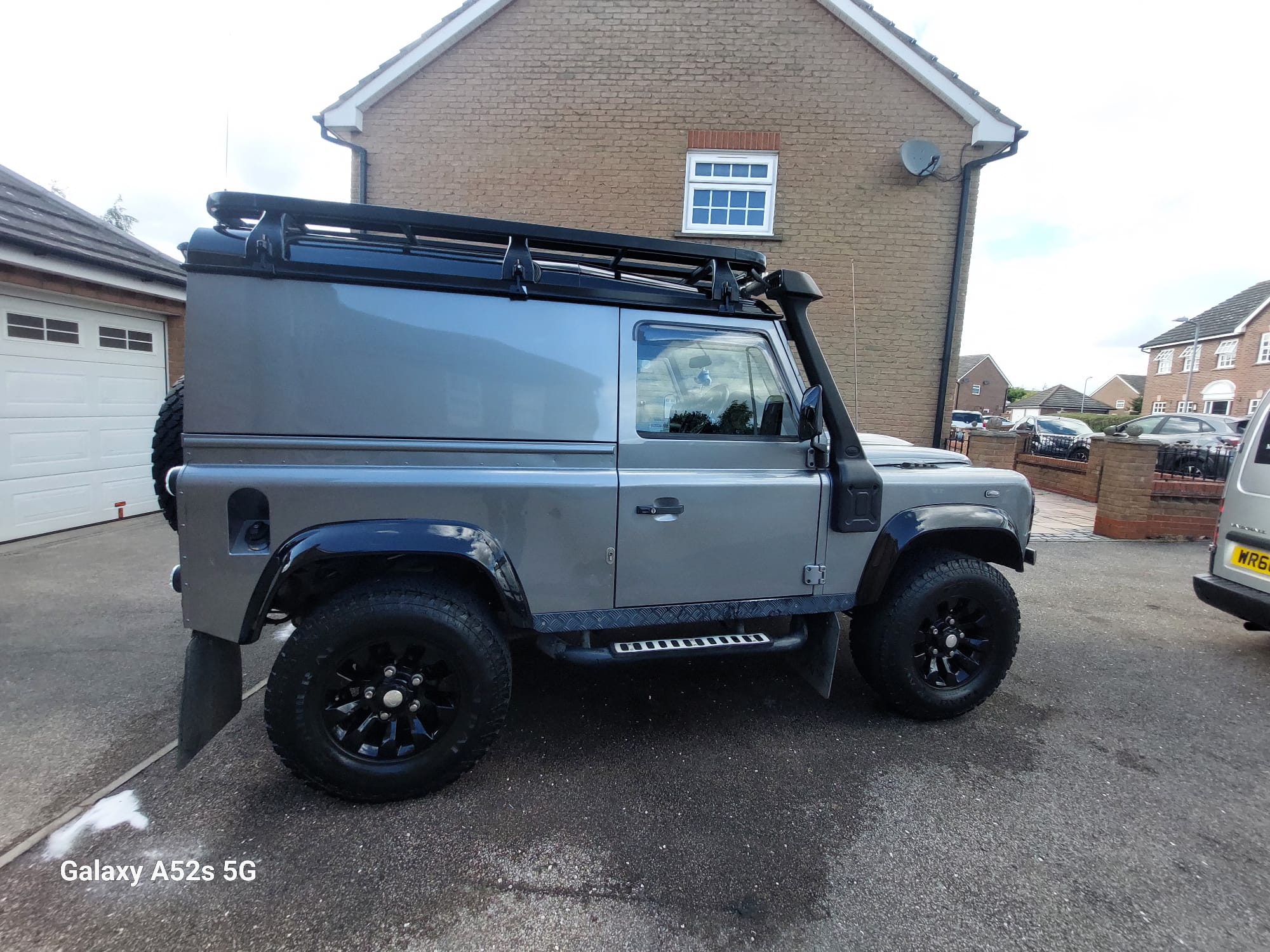 Grey Land Rover Defender 90 with roof rack detailed on a driveway