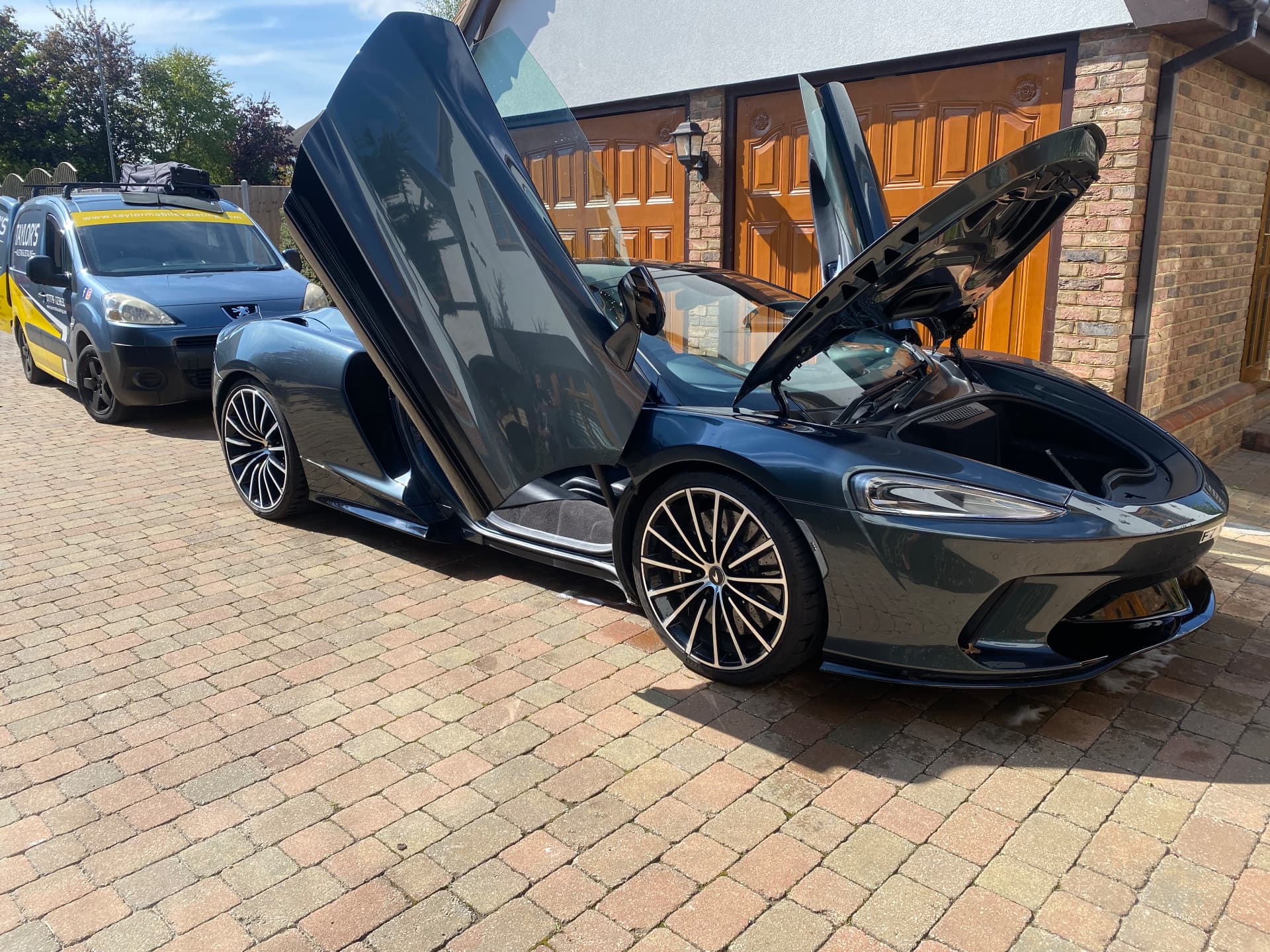 Freshly detailed McLaren GT with doors open on a driveway beside the Taylor's mobile valeting van