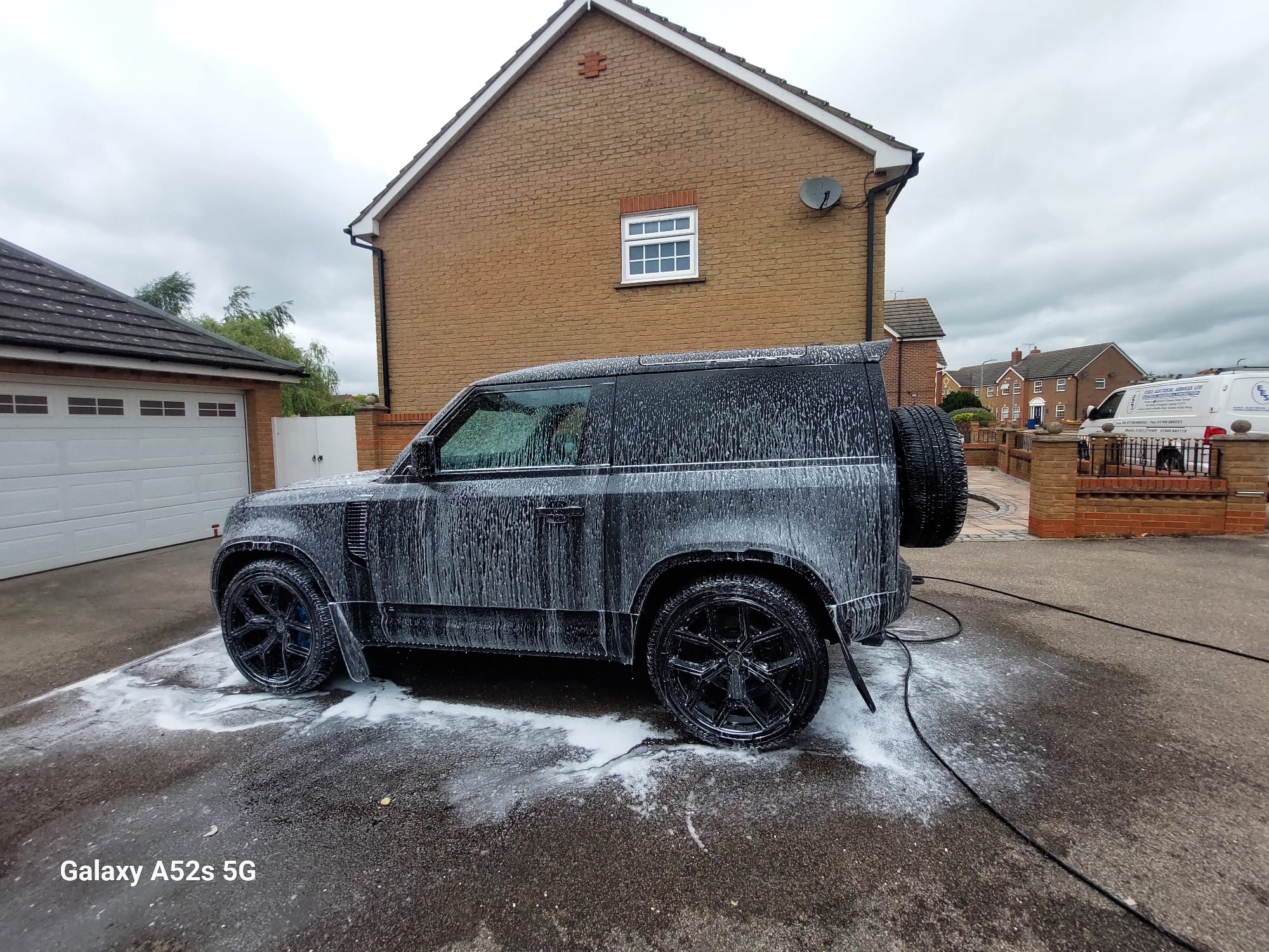 Black Land Rover Defender covered in snow foam during a driveway wash
