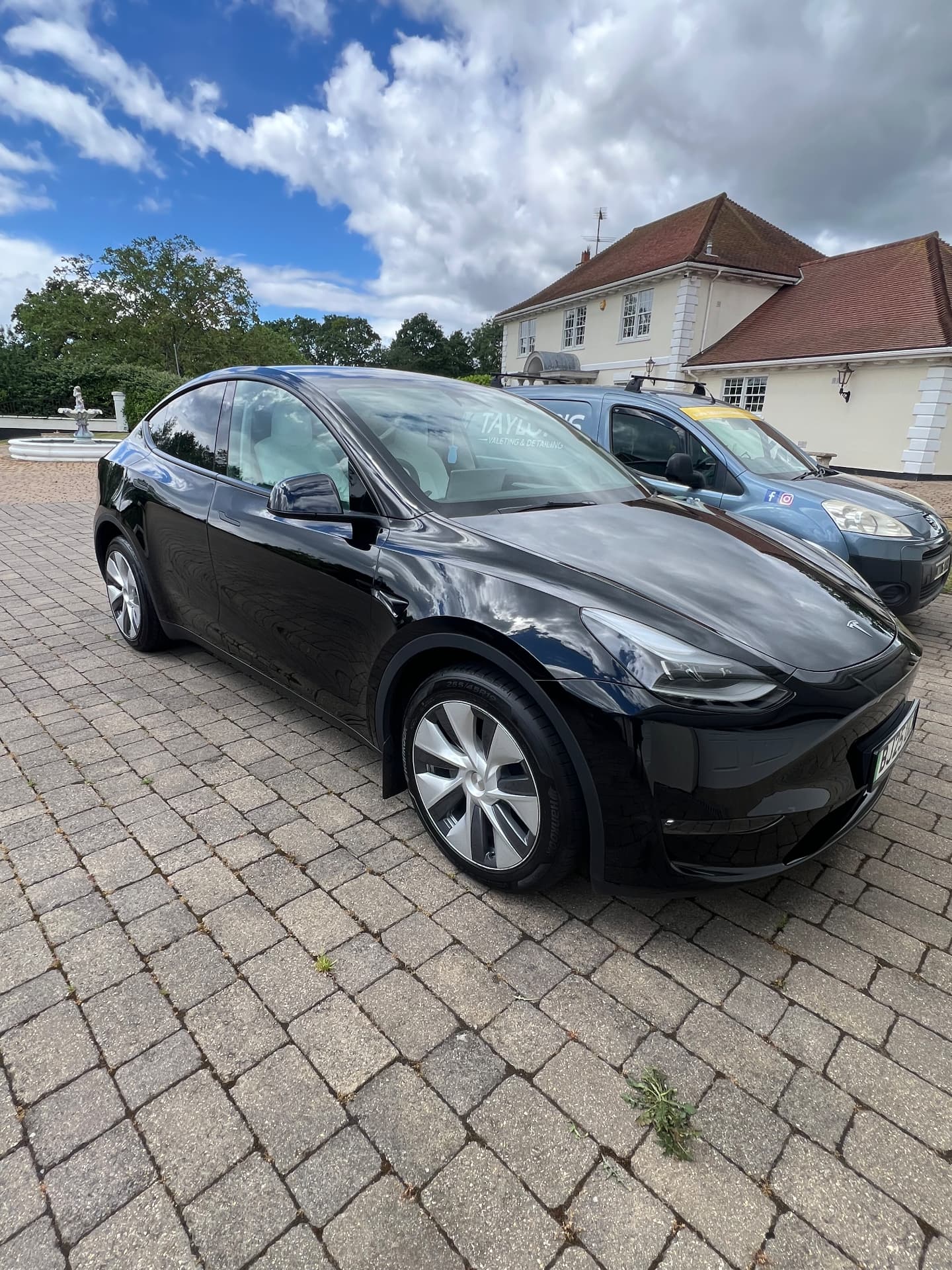 Black Tesla Model Y detailed on a driveway beside the Taylor's valeting van