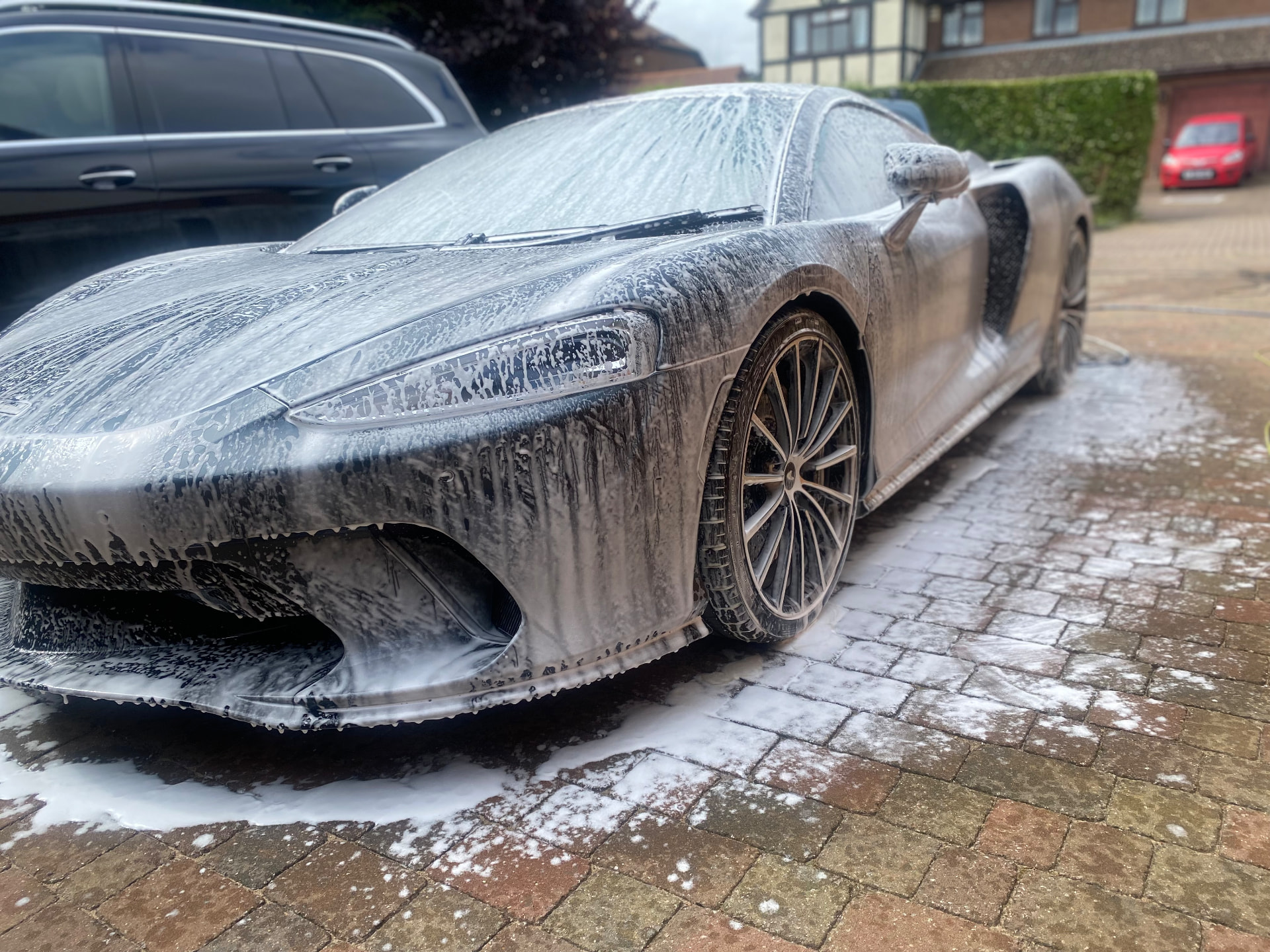 Grey McLaren GT covered in snow foam on a block-paved driveway